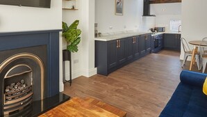 A modern living room with a fireplace, a dining area, and a kitchen with dark cabinets and a white countertop. - Host Stay Montrose View (Saltburn-by-the-Sea)