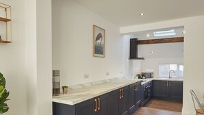 A modern kitchen with dark cabinets, a marble countertop, and a built-in oven. - Host Stay Montrose View (Saltburn-by-the-Sea)