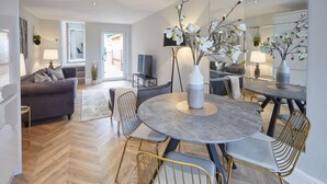 A modern living room with a round dining table, grey sofa, and a large mirror reflecting the room. - Host Stay The Madison at Prospect Hill Apartments (Whitby)