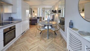 A modern kitchen with white cabinetry, a built-in oven, and a herringbone wood floor. There is a dining area with a round table and chairs, and a large mirror on the wall. - Host Stay The Madison at Prospect Hill Apartments (Whitby)