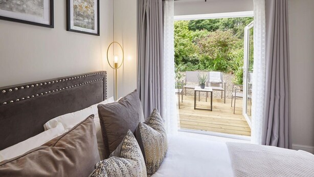 A bedroom with a large bed, a view of an outdoor patio with a table and chairs, and two framed artworks on the wall. - Host Stay The Madison at Prospect Hill Apartments (Whitby)