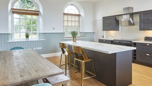 Een ruime keuken met een groot eiland, houten vloeren en uitzicht op de omgeving door boogvensters.