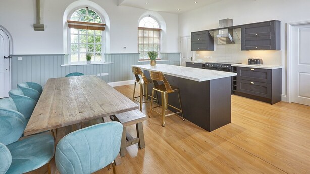 Een moderne keuken met een houten eettafel en teal-kleurige stoelen, een centraal kookeiland en donkere kastjes.