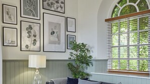 Een woonkamer met een grijze bank, een lamp en kunstwerken in lijsten aan de muur.