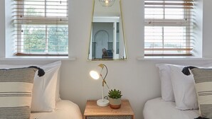 Een slaapkamer met twee bedden, een nachtkastje met een lamp, een spiegel en een raam met zonwering.