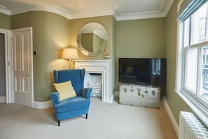 A living room with a blue armchair, a fireplace, a television, and a large window. - Host Stay Henderson House (Whitby)