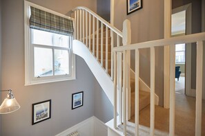 Stairs lead to an upper floor, flanked by framed pictures on neutral-toned walls.