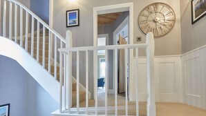 A staircase with white railings leading to a second floor, a large wall clock, and framed pictures on the walls. - Host Stay Henderson House (Whitby)