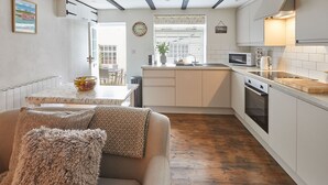 A compact kitchen with white cabinets, a microwave, and a sink. There's a dining area with a table and chairs, and a sofa with cushions. - Host Stay Dolphin Cottage 1736 (Whitby)