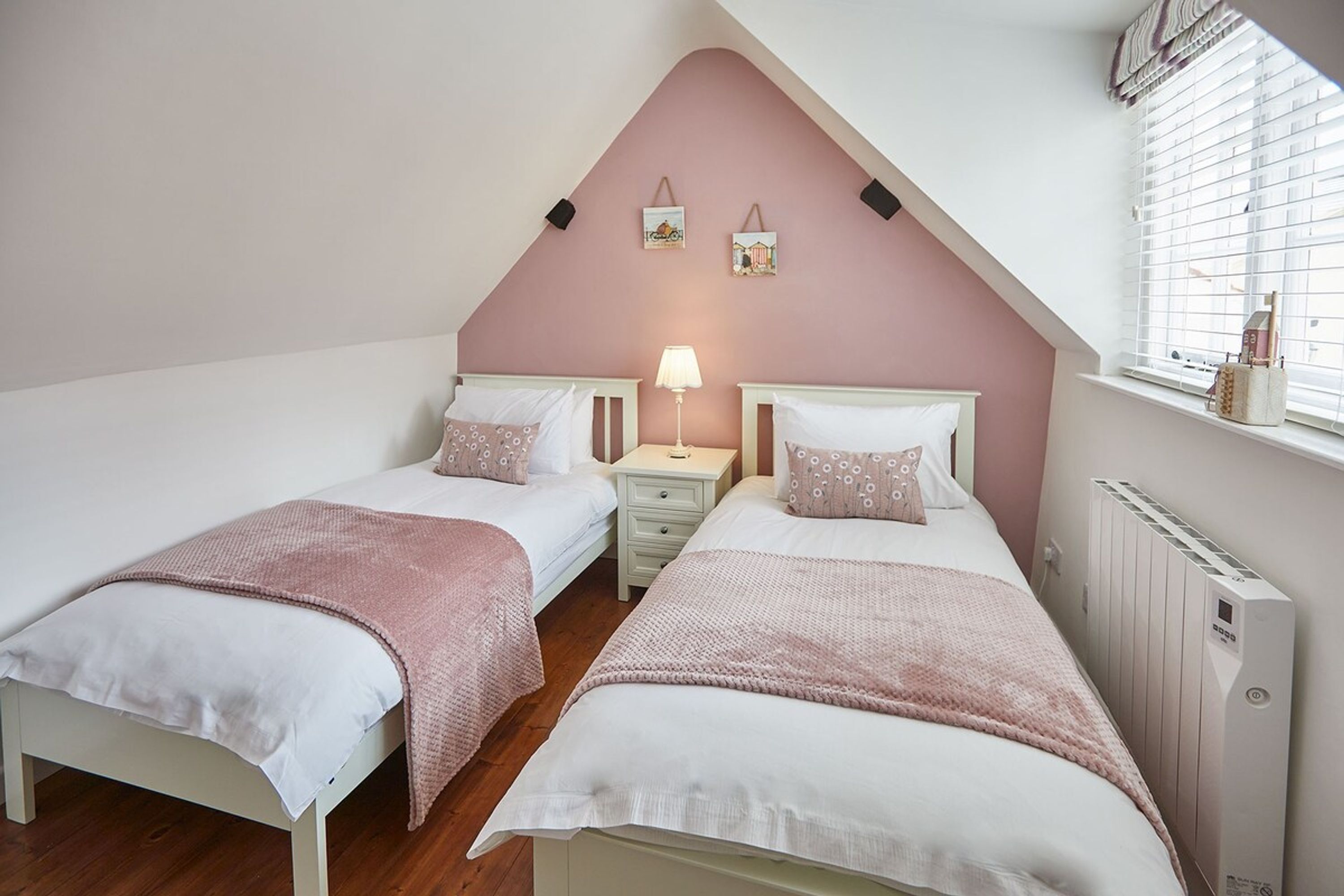 A bedroom with two beds, a nightstand, a lamp, and a window with blinds.