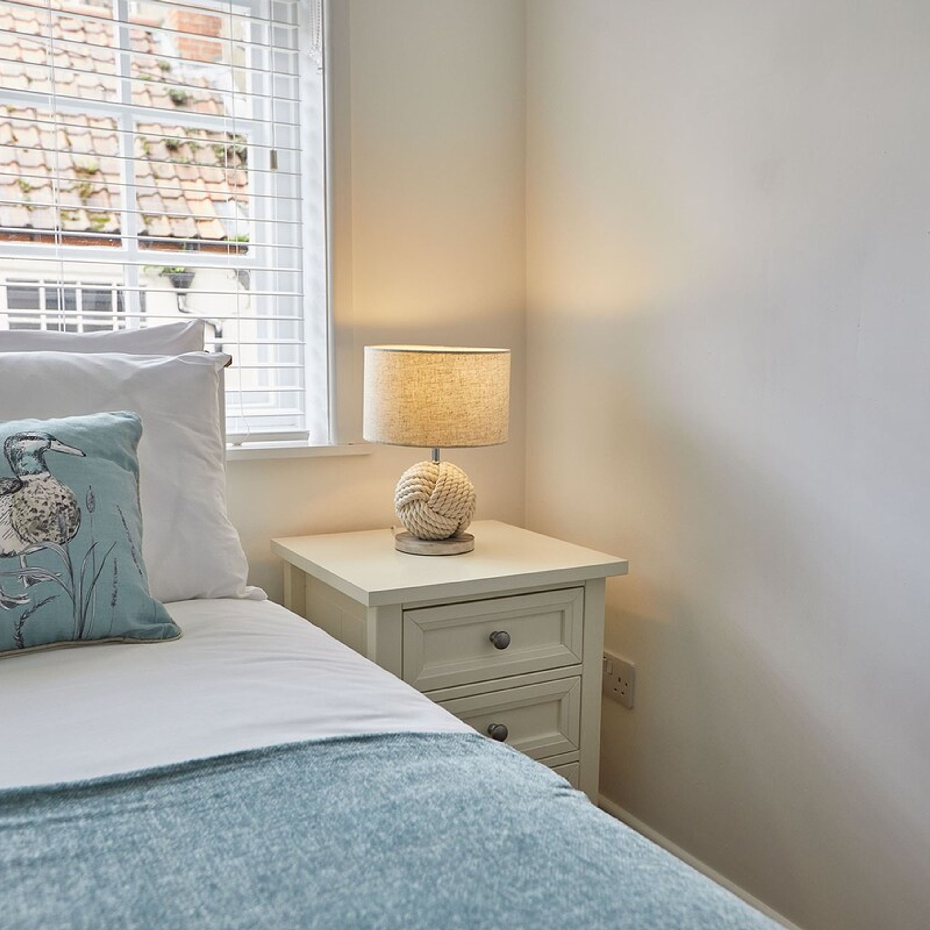 A bedroom with a bed, a nightstand with a lamp, and a window with blinds.