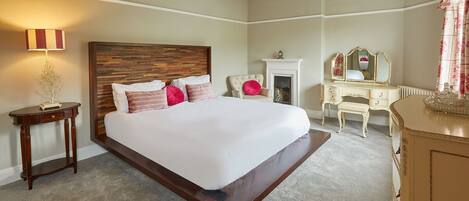 A bedroom with a large bed, a dresser, a chair, a lamp, and a fireplace.