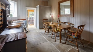 Uma área de jantar com uma mesa e cadeiras de madeira, um espelho grande e piso de pedra.