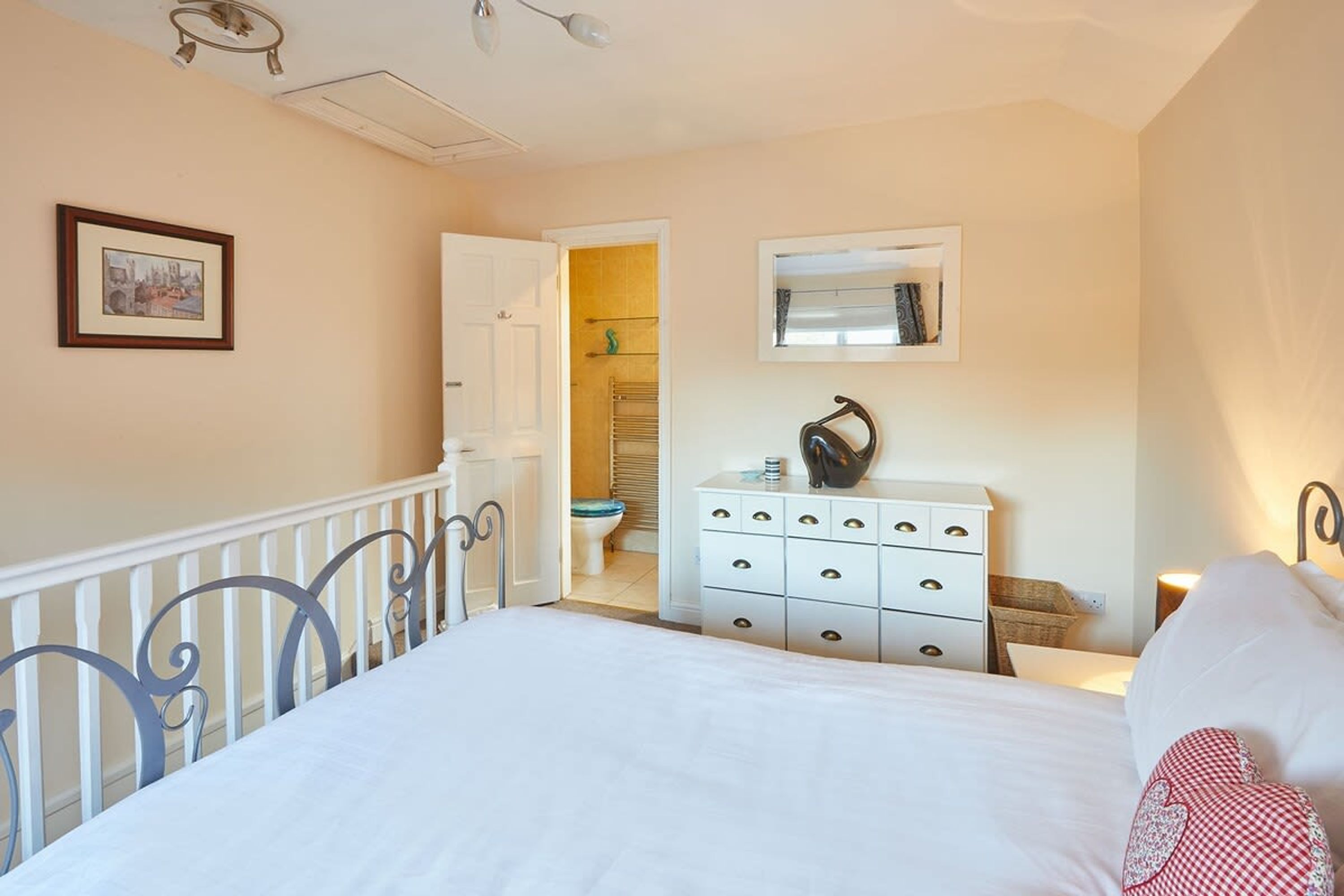 A bedroom with a bed, a dresser, a mirror, and a door leading to a bathroom.