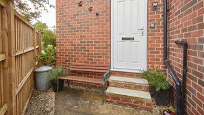A brick house with a white door, a wooden fence, a bench, and potted plants. - Host Stay The Limes (Harrogate)