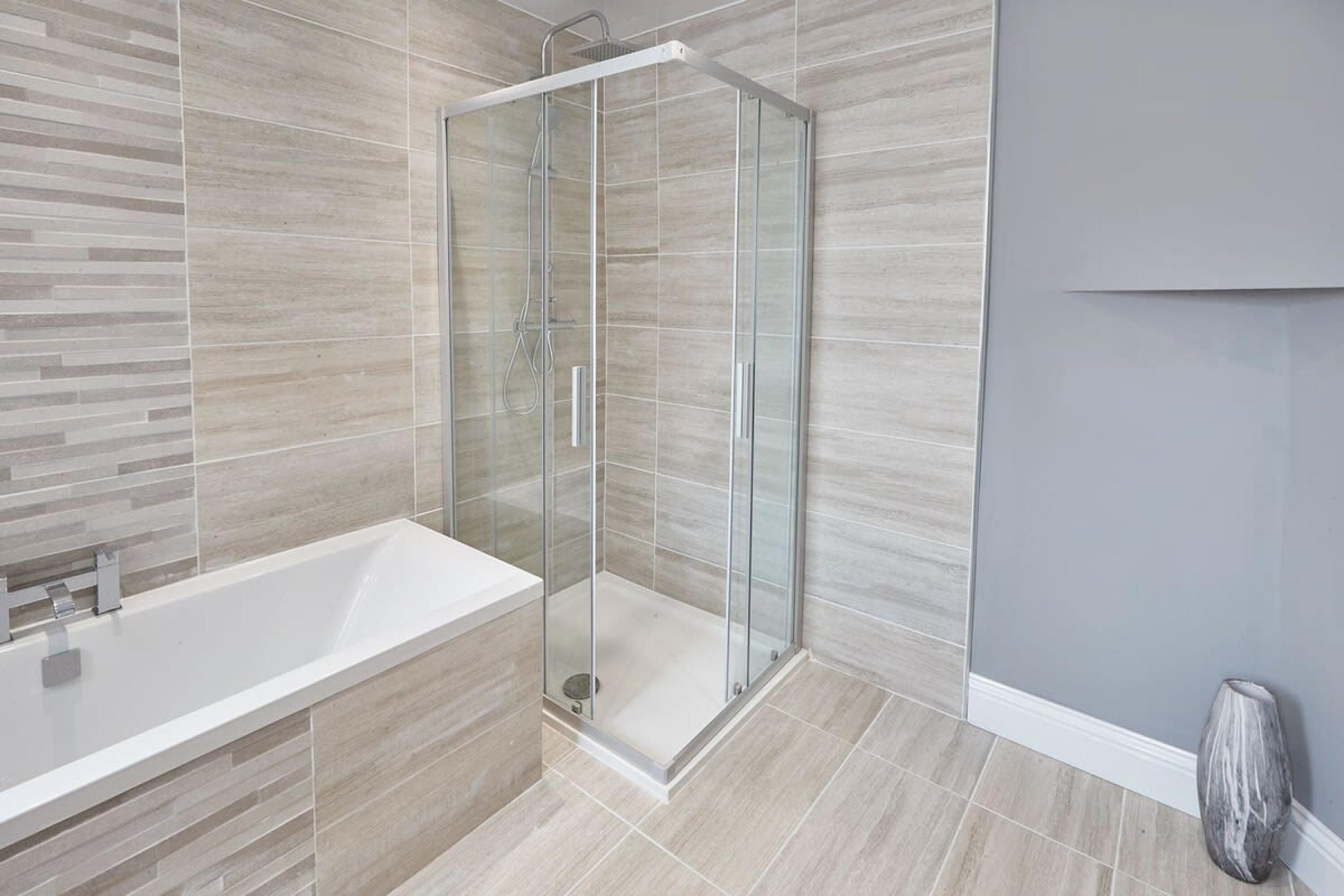 A modern bathroom with a glass-enclosed shower, a white bathtub, and light-colored tiles.