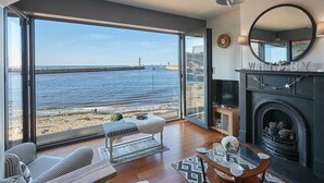 A spacious living room with a large bay window overlooking a beach and the sea. - Host Stay No 3 Sandside (Whitby)