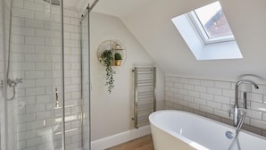 Une salle de bain moderne dotée d’une douche à parois de verre, d’une baignoire sur pieds et d’un puits de lumière.