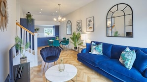 Un salon moderne avec un canapé bleu, une table basse ronde et un escalier menant à l’étage supérieur.