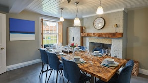 Ein Esszimmer mit Holztisch, gedeckten Plätzen für sechs Personen, blauen Stühlen, einem Kamin und einer Wanduhr.