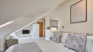 Een moderne slaapkamer met een groot bed, een flatscreen televisie aan de muur en een gezellige zithoek met een gestreept poef.