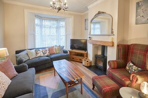 A cozy living room with a sofa, a wooden coffee table, a plaid armchair, and a fireplace.