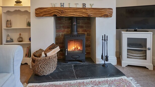 A cozy living room with a fireplace, a television, and a bookshelf. - Host Stay Tenby Cottage (Whitby)