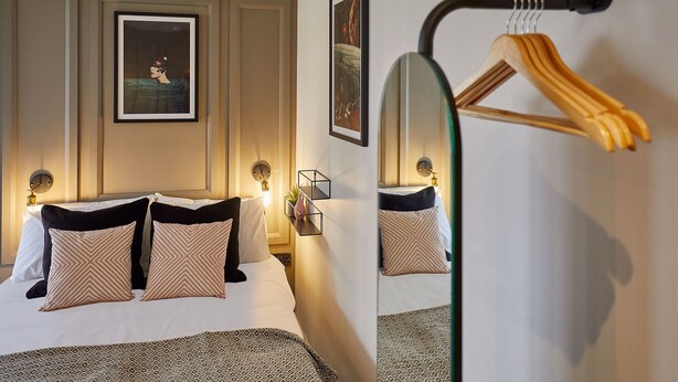 Ein Hotelzimmer mit einem Bett, zwei gerahmten Bildern an der Wand, einem Spiegel und einem hölzernen Kleiderhaken.