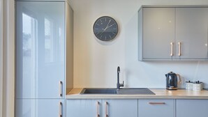 Eine Küche mit Spüle, Schränken, einer Uhr und einem Wasserkocher.