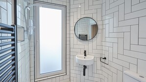 Ein Badezimmer mit Fischgrätmuster, einem weißen Waschbecken, einem runden Spiegel und einer Dusche mit Glastür.
