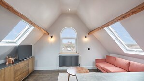 Une chambre à coucher aménagée dans un espace ouvert, avec des fenêtres de toit, un canapé, une télévision et une table à manger.
