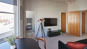 Un salon moderne avec une grande fenêtre, un téléviseur à écran plat, un trépied et une plante en pot.