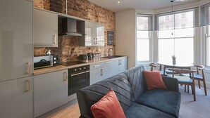 Une cuisine moderne avec un mur en briques, des meubles gris et un canapé gris agrémenté de coussins rouges.