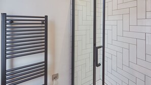 Une salle de bain dotée d’une porte de douche en verre, d’un porte-serviettes noir et d’un mur carrelé avec un motif en chevrons.