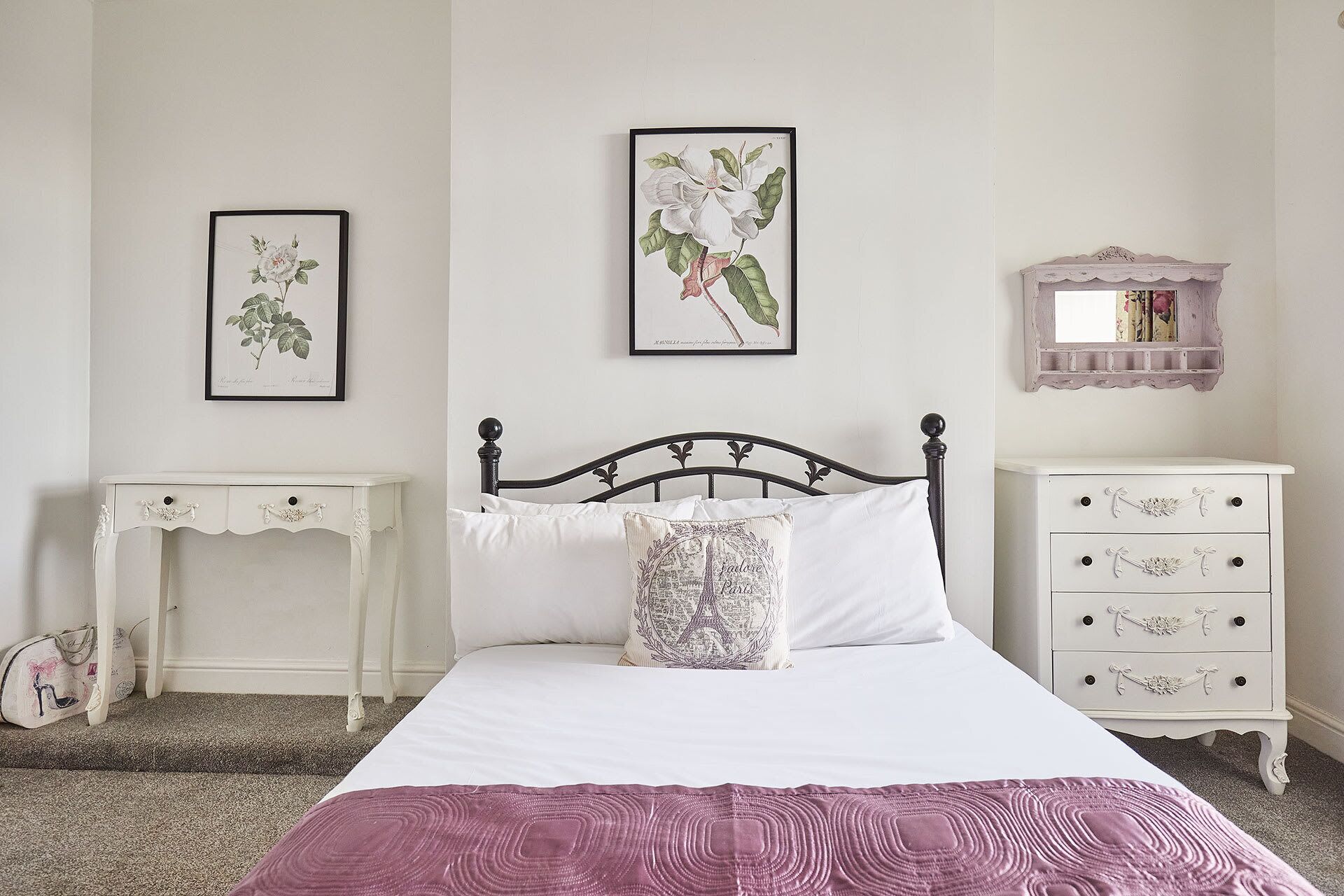 Een slaapkamer met een bed, twee nachtkastjes, een dressoir en twee ingelijste afbeeldingen van planten aan de muur.