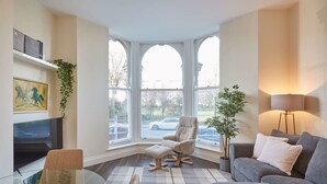 Un salon moderne avec une table basse en verre, un canapé gris, un fauteuil beige et un téléviseur posé sur un meuble blanc.