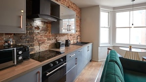 Una cocina moderna con pared de ladrillo, electrodomésticos de acero inoxidable y un sofá verde en la zona de estar.