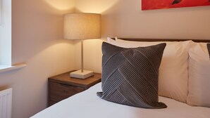 Una cama bien hecha, con un cojín estampado y una lámpara de noche sobre una mesita de madera.