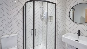 Une salle de bain moderne avec une douche à parois de verre, un lavabo blanc et un mur recouvert de carreaux disposés en motif chevrons.