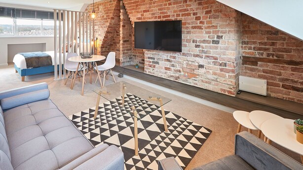 Un salon moderne avec un mur en briques, un téléviseur à écran plat, un coin repas avec une table ronde et des chaises, et un canapé.