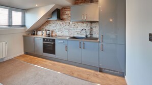 Une cuisine moderne avec des meubles gris, une cuisinière noire et un mur en briques.