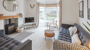 A modern living room with a sofa, a television, a fireplace, and a large window with curtains. - Host Stay Retreat By The Sea (Redcar)