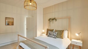 A bedroom with a bed, bedside tables, a hanging light fixture, and a door. - Host Stay Retreat By The Sea (Redcar)