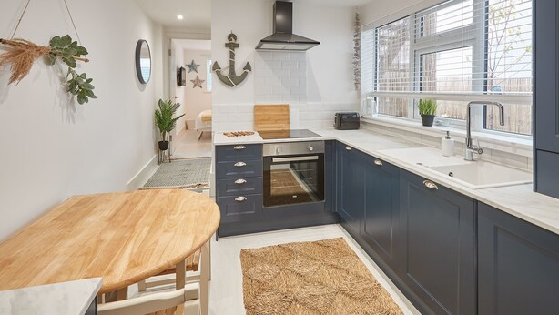 A modern kitchen with dark blue cabinets, a wooden table, and a built-in oven. - Host Stay Retreat By The Sea (Redcar)
