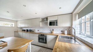 A modern kitchen with white cabinetry, a wooden countertop, a built-in oven, a microwave, and a window providing natural light. - Host Stay Great Habton Cottage (Malton)