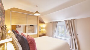 A bedroom with a large bed, a wooden wardrobe, a desk with a lamp, and a window with curtains. - Host Stay Great Habton Cottage (Malton)