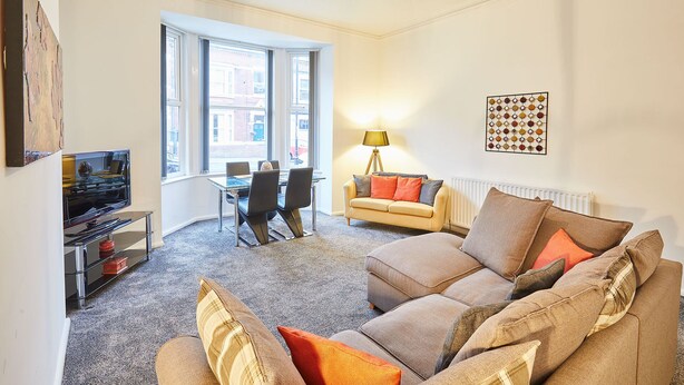 A living room with a sofa, a coffee table, a dining table with chairs, a lamp, and a wall-mounted artwork. - Host Stay Diamond One (Saltburn-by-the-Sea)