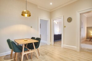 A dining area with a wooden table and green upholstered chairs, a gold pendant light, and a clock on the wall. - Host Stay Huntcliff View Apartment (Saltburn-by-the-Sea)