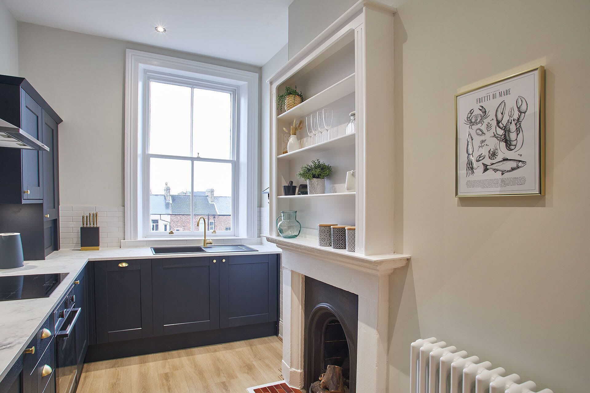 A modern kitchen with dark cabinetry, a white countertop, a large window, and a fireplace.