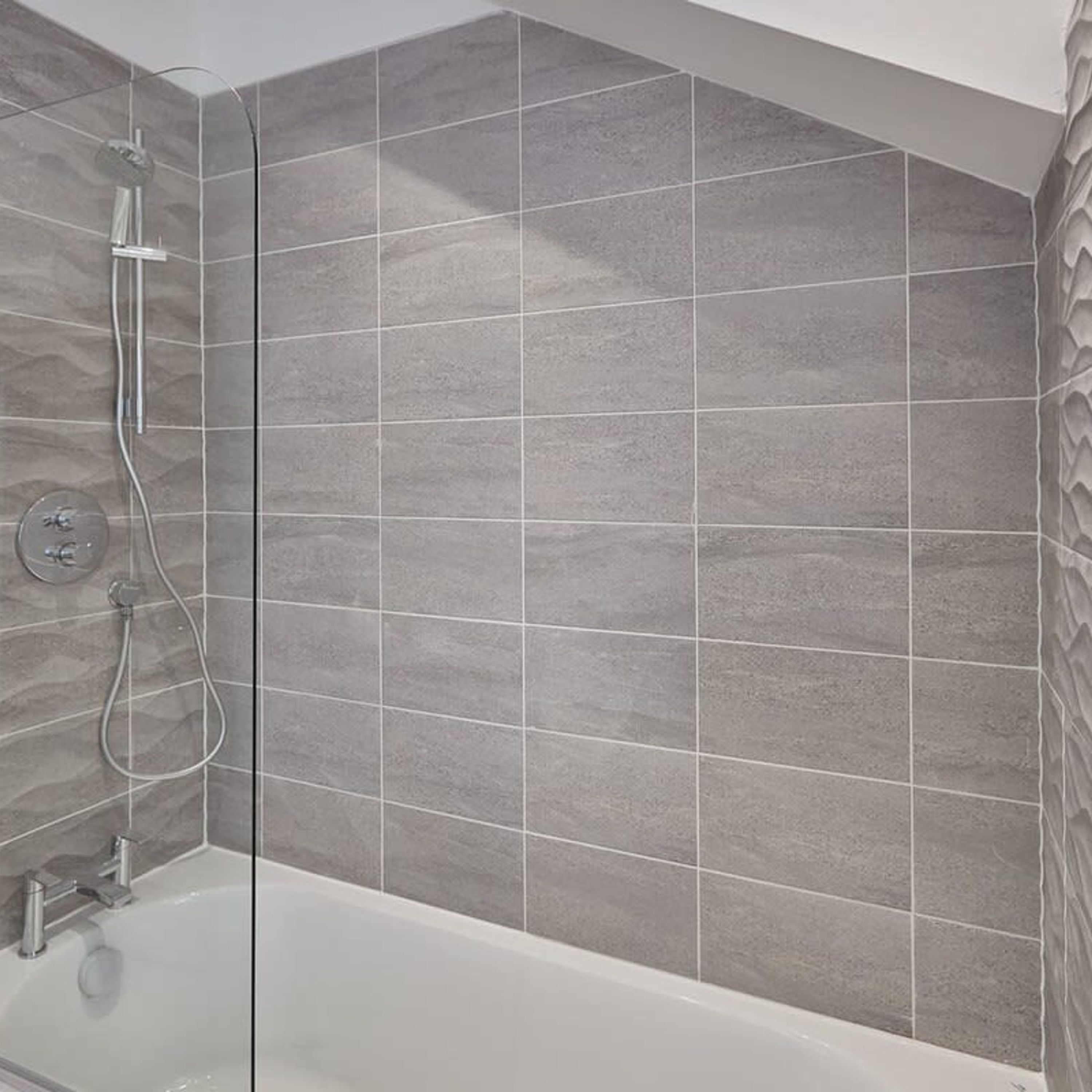 Een moderne badkamer met een bad, douche en betegelde wanden.